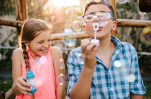 Happy teenage boy and girl having fun outdoors blowing soap bubbles