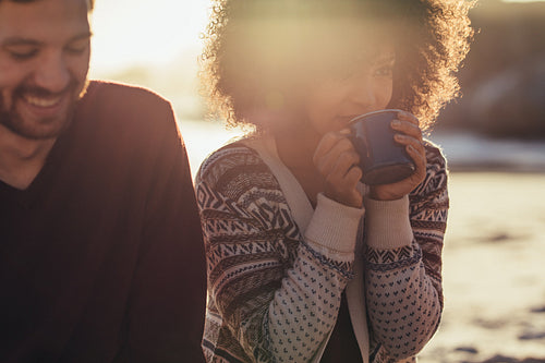 Woman having coffee with friend sitting by at beach