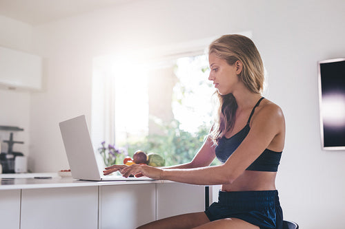 Beautiful woman sitting by kitchen counter and using laptop
