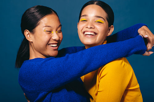 Feeling happy in makeup, two female friends embrace each other in a studio