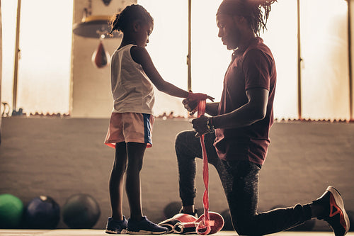 Side view of a boxing coach wrapping bandage on hands of a kid