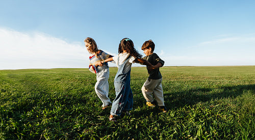 Diverse children holding hands and playing together in open field