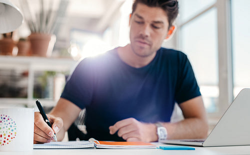 Young man sitting at desk writing notes