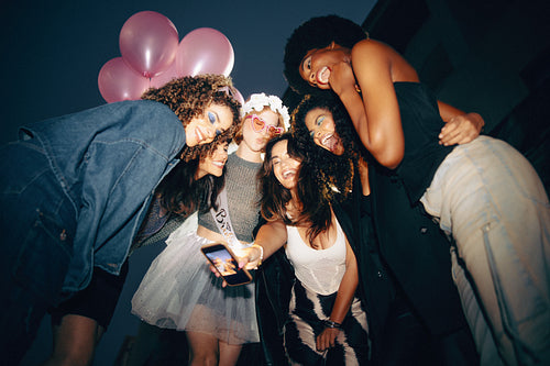 Group of friends celebrating together at night with balloons, laughter, and taking a selfie