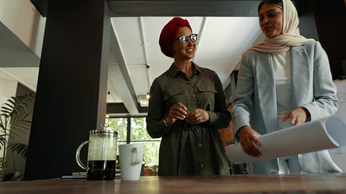 Architects wearing headscarves reviewing blueprint drawings in an office