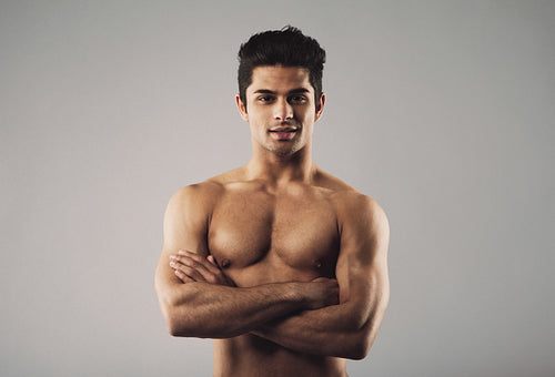 Bare-chested muscular man standing on grey background