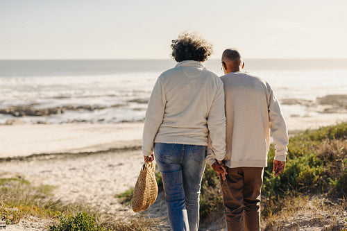 Rearview of a romantic senior couple going to the beach for a picnic