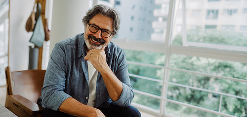 Senior man sits indoors by a window at home