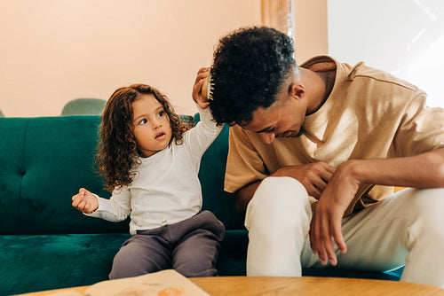 Cute little girl combing her father's hair at home