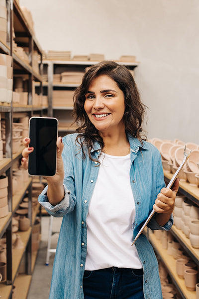 Successful ceramist showing a blank smartphone screen in her shop