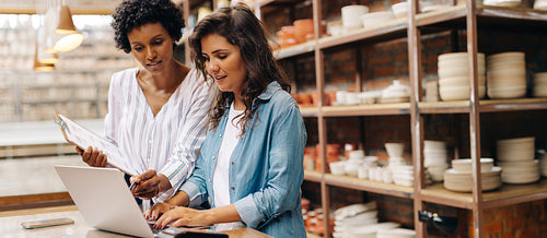 Female ceramists using a laptop together in their shop