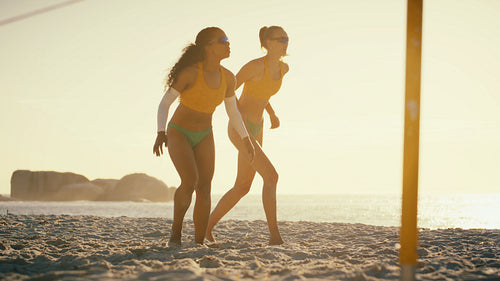Professional female beach volleyball players high five during sunset game