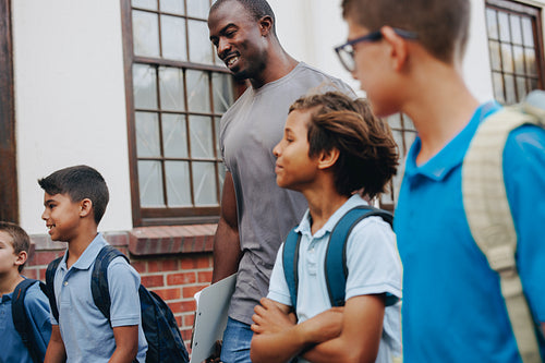 Male school teacher walking outside class with his students