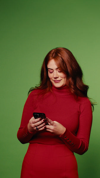 Woman in red dress smiles at phone on green screen