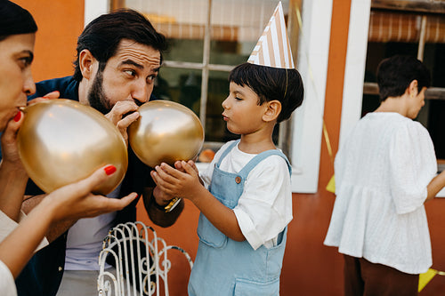 Family celebrating a birthday outdoors with balloons and party hats
