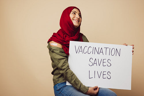 Muslim woman in hijab holding "Vaccination saves lives" banner
