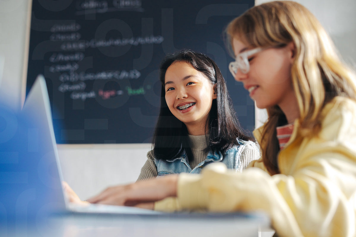 Happy young girls sitting in a coding class, learning basic programmin ...
