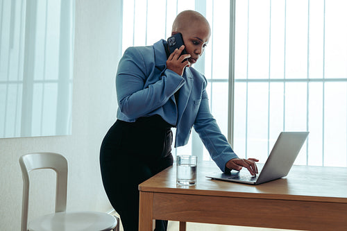 Focused businesswoman multitasking with a phone call and laptop in a modern office