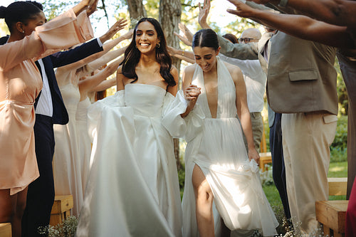 Lesbian brides celebrate their marriage surrounded by cheering guests in outdoors ceremony