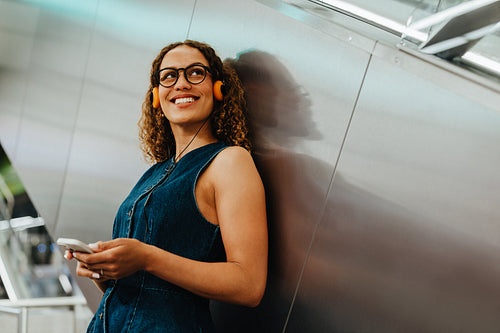 Smiling woman with headphones checks departure screen in transit station