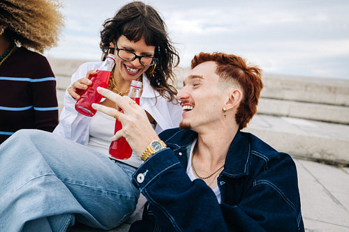Gen Z friends laughing while sharing drinks on steps