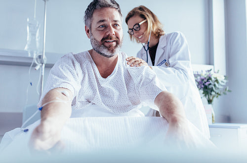 Mature man sitting in hospital bed and physician doing checkup.