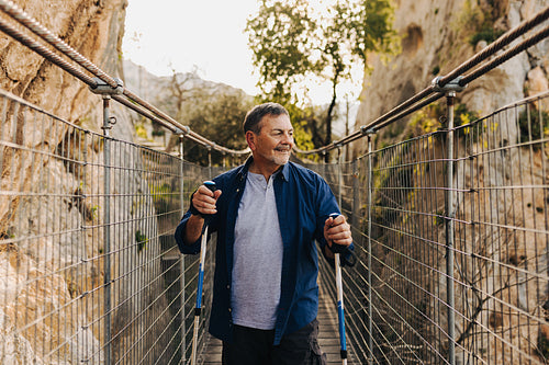 Adventurous senior man crossing a bridge with hiking poles