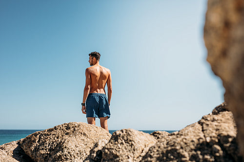 Man standing on top of rocks looking at the sea