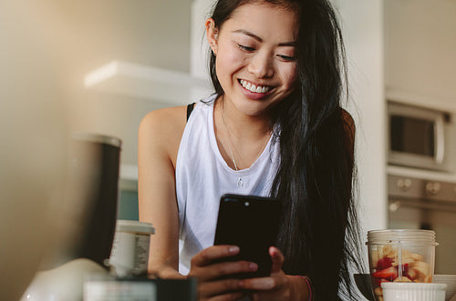 Smiling female with smartphone in kitchen in morning