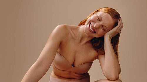 Smiling woman relaxed with hand supporting head in nude tones