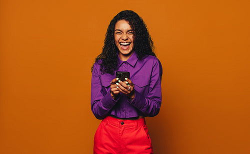 Smiling woman using phone on orange background