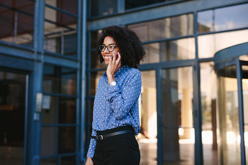 Businesswoman walking out of the office building talking on phone