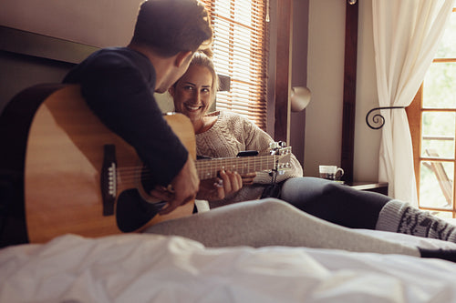 Man playing guitar for his girlfriend in bed