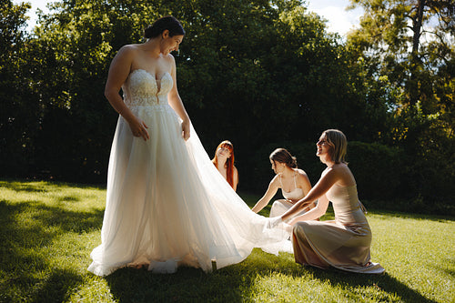 Bride with bridesmaids adjusting dress in an outdoor setting