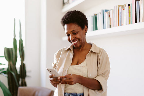 Happy black woman reading text message on smartphone in her living room