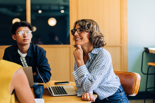 Smiling professionals in casual meeting setting with laptops and coffee nearby