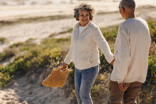 Happy senior woman holding her husband by the hand at the beach