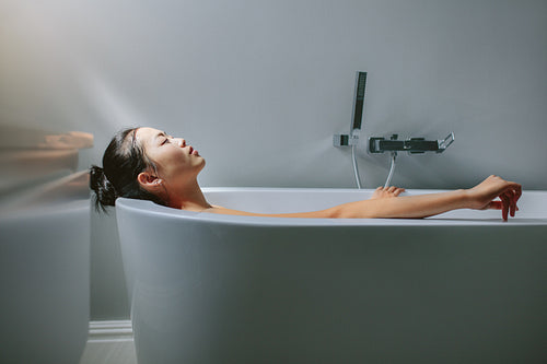 Asian female lying in bathtub