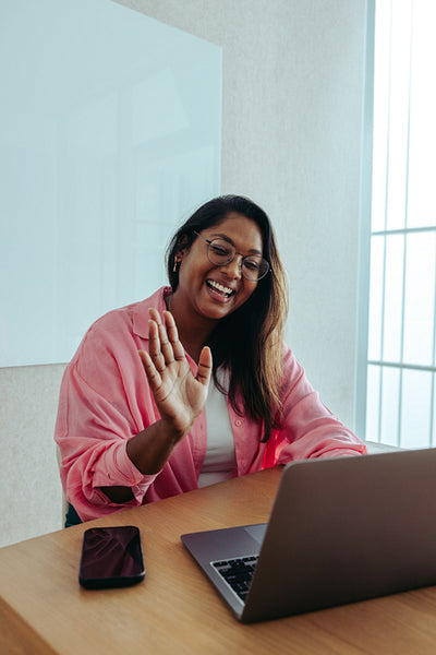 Indian businesswoman greeting client in virtual meeting with laptop and smartphone