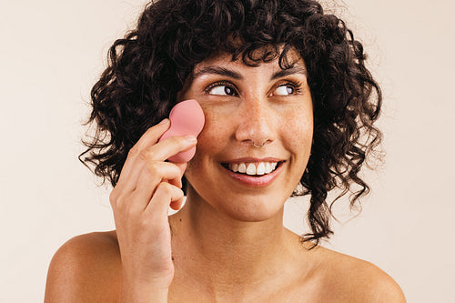 Pretty woman using a beauty blender on her face