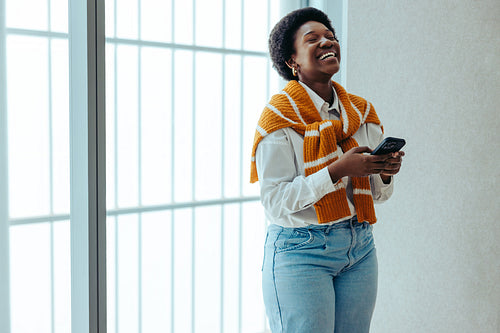 Laughing woman using smartphone while standing in a bright office space
