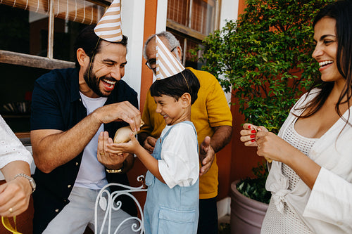 Family enjoying a birthday celebration outdoors together with party hats and balloons