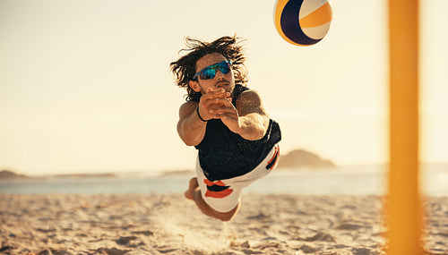 Dynamic athlete soars mid air in competitive volleyball match on coastal sand court