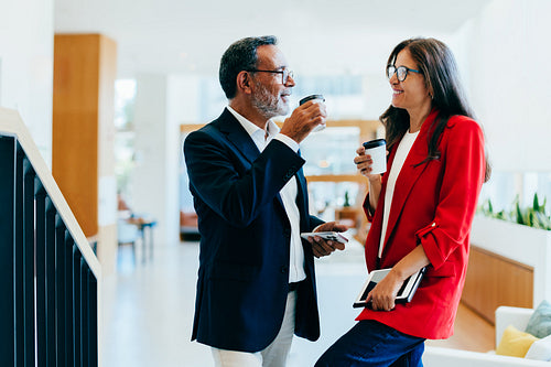 Two senior professionals enjoying coffee and conversing in a bright office space