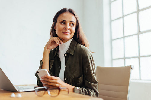 Thoughtful business woman holding a mobile phone in her office
