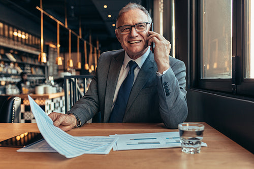 Smiling senior businessmen at cafe talking over phone