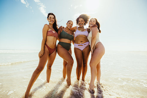 Happy female friends standing on beach water