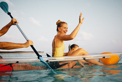 Woman waving while rowing a canoe with an oar on calm waters