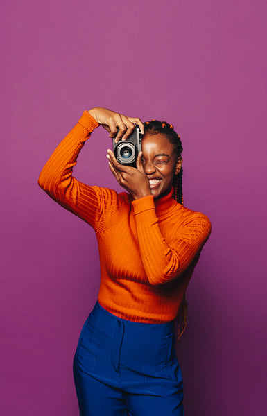 Cheerful female photographer capturing vibrant picture on purple background