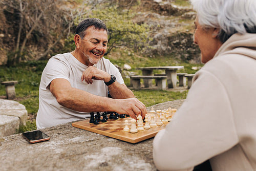 Easygoing senior couple playing chess together in a park
